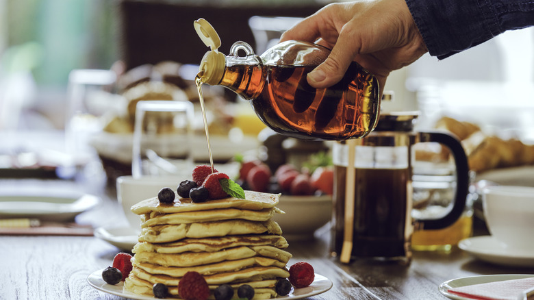 Someone pouring maple syrup on pancakes