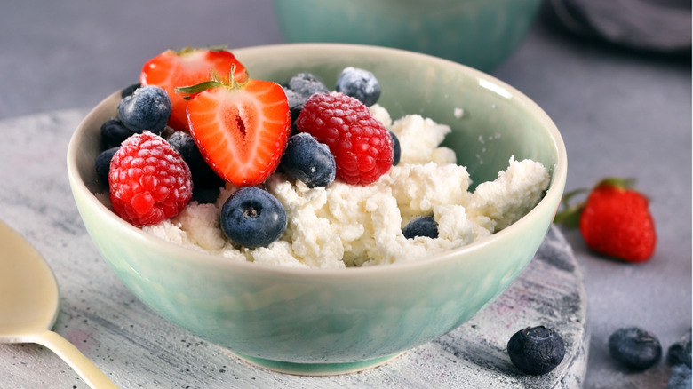 Blue bowl of cottage cheese with strawberries on a white plate on a table.