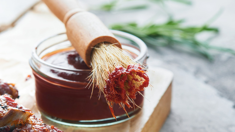A glass jar of barbecue sauce with a wet basting brush