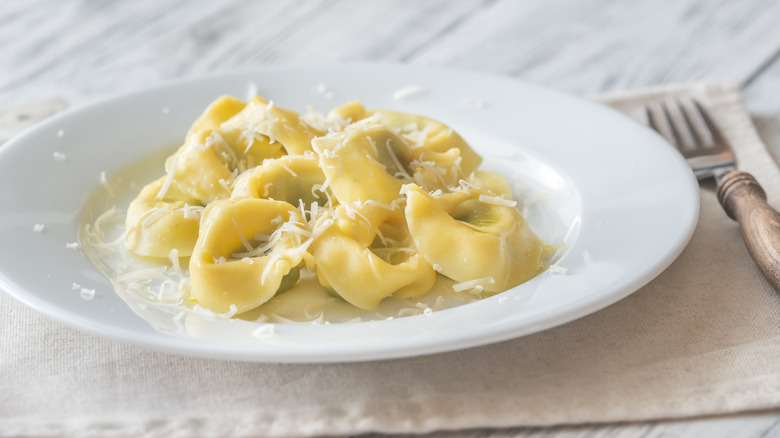 White plate of tortelloni with parmesean cheese on a marble table with a fork.