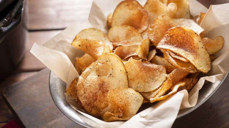 Seasoned potato chips in a silver dish with parchment paper on a table