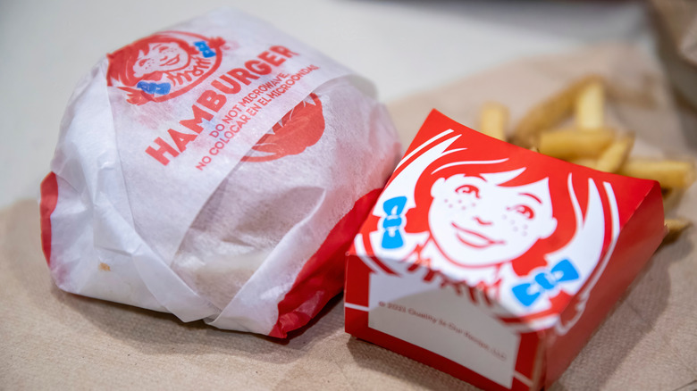 A Wendy's burger in paper wrapping next to a small order of fries