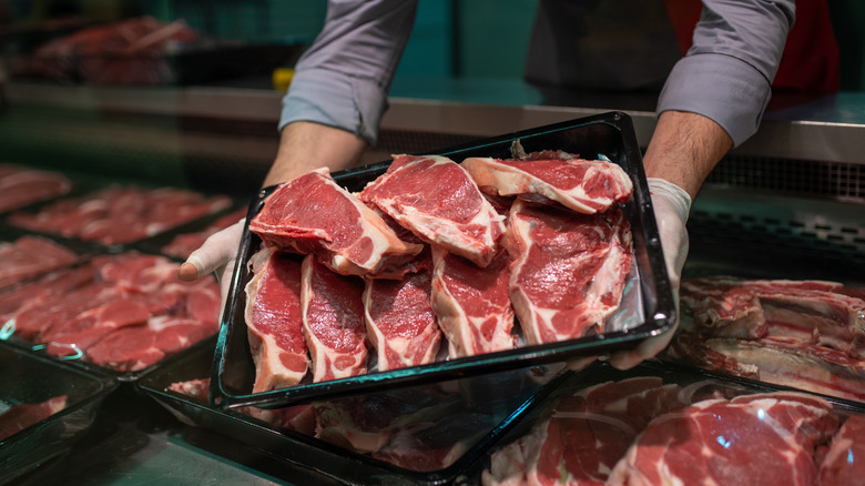 Closeup of a butcher's hands holding a tray of meat pieces.