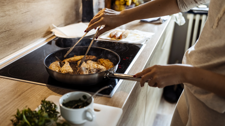 Woman cooking fish with tongs on stove