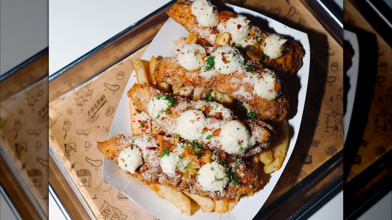 Three Sticky's chicken tenders topped with white sauce on a bed of fries