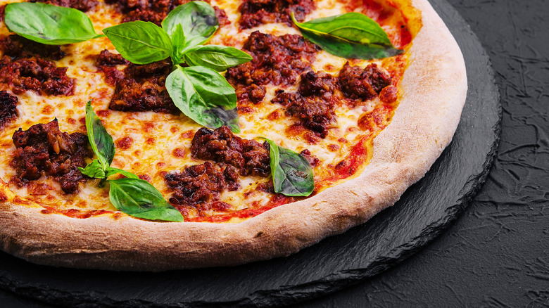 Meat and basil pizza on a black pizza stone