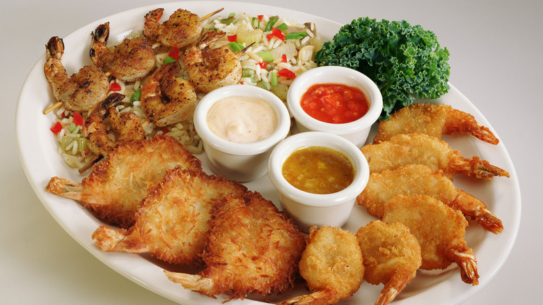 Plate of shrimp skewers, coconut shrimp, and fried shrimp with three sauces and garnish