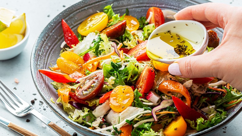 Hand pouring olive oil over salad