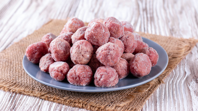 frozen meatballs piled on a white plate sitting on a white wood tabletop