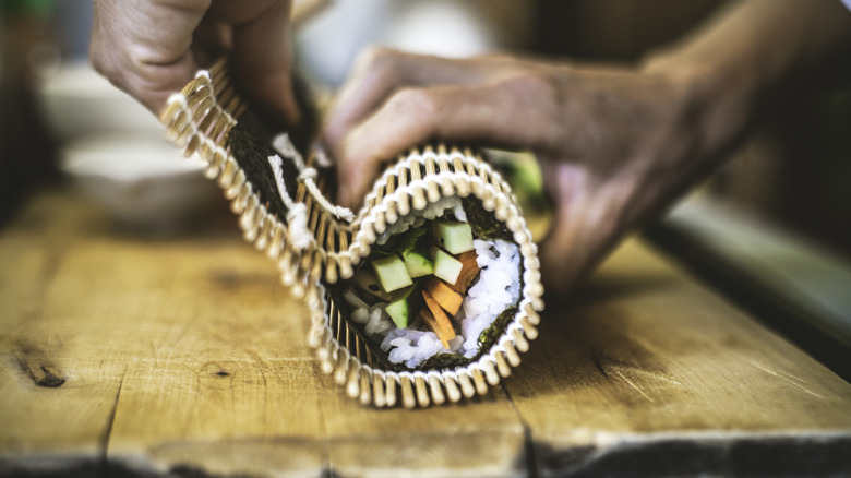 hands of a sushi chef rolling up a sushi roll