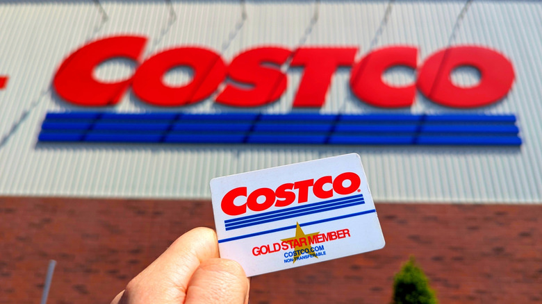 Hand holding Costco membership card with sign in background