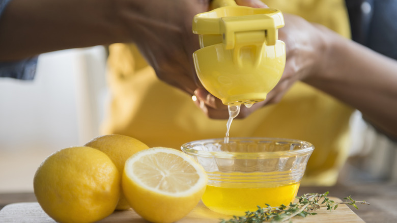 Person using a lemon juice squeezer to squeeze lemon juice into a glass bowl with lemons on the table.