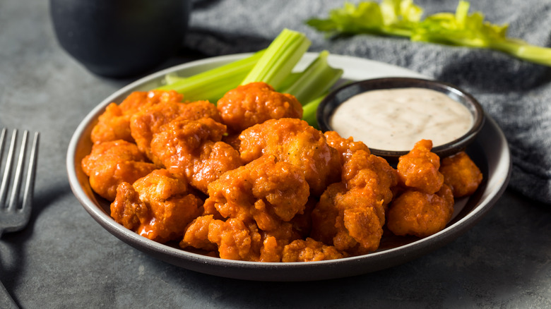 A bowl of boneless Buffalo wings with celery sticks and a side of ranch dressing