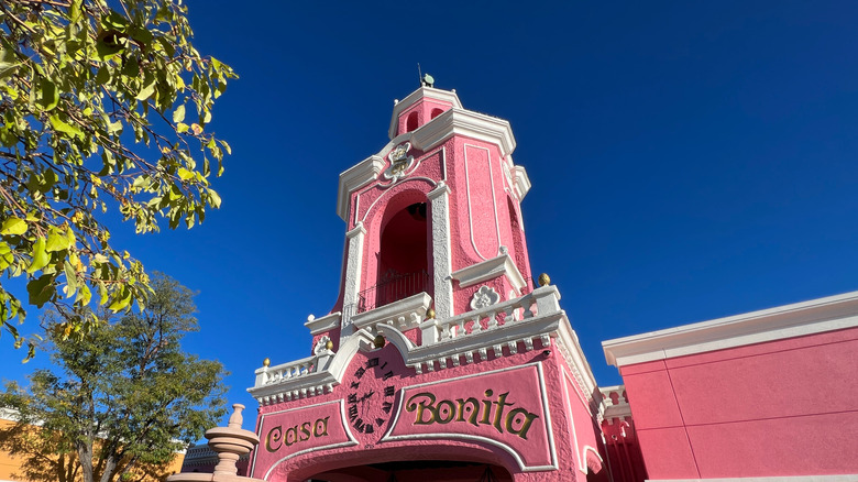 The exterior of Casa Bonita, a bright pink building with white accents, gold lettering, and a bell tower