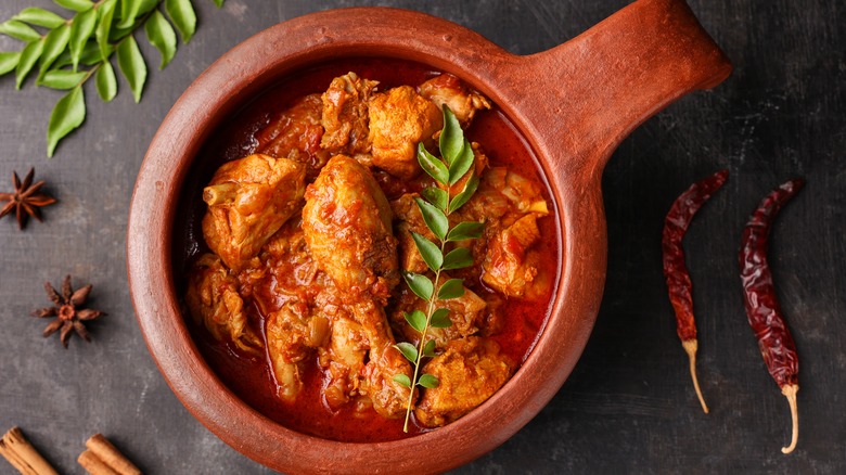 A wooden bowl with spicy red chicken curry topped with herbs