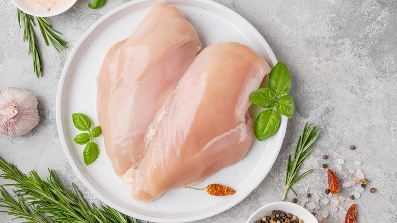 raw chicken on white plate wth herbs