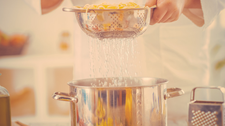 straining pasta into a pot in kitchen