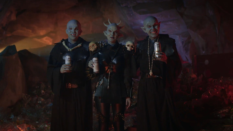 Actors in full demon makeup and costuming, smiling with cans of Liquid Death