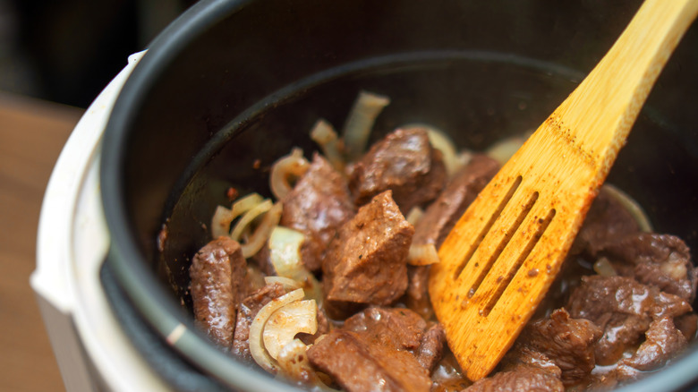 Beef tips and chopped onions in an open pressure cooker