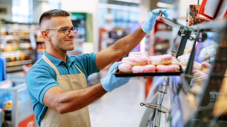 supermarket bakery employee restocking donuts in a case
