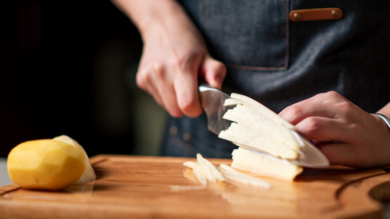 hand cutting potatoes on wooden cutting board