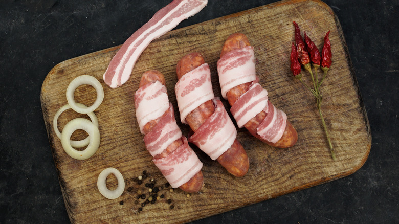raw bacon-wrapped bratwurst on wooden cutting board
