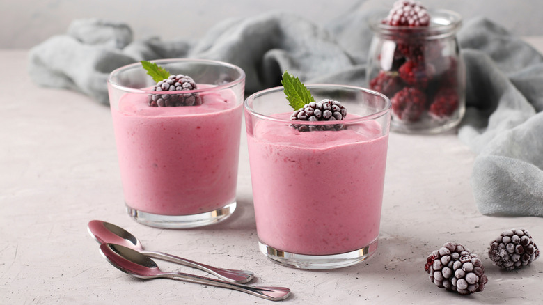 Two frozen fruit smoothies with frozen blackberries and spoons