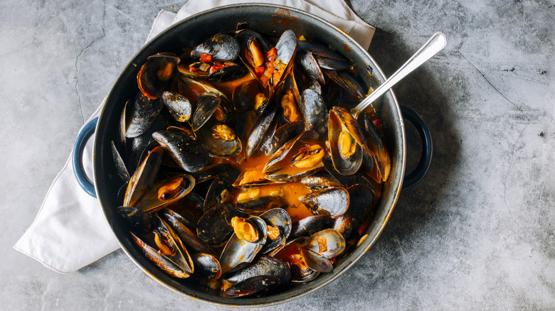 Pot filled with mussels on gray background