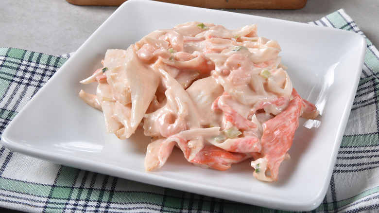 Creamy seafood salad on a white dish on a cloth napkin on a table.