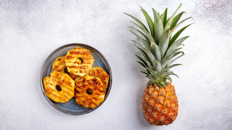 A plate of grilled pineapple beside a whole one 