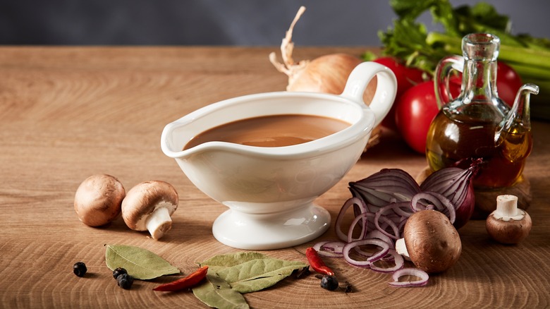 Gravy boat with herbs, oil, vegetables beside it