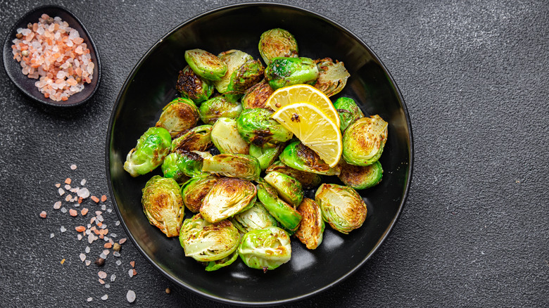 Bowl of crispy roasted Brussels sprouts with lemon and a small bowl of sea salt