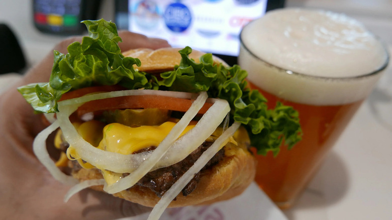 Hand holding Smashburger beside beer