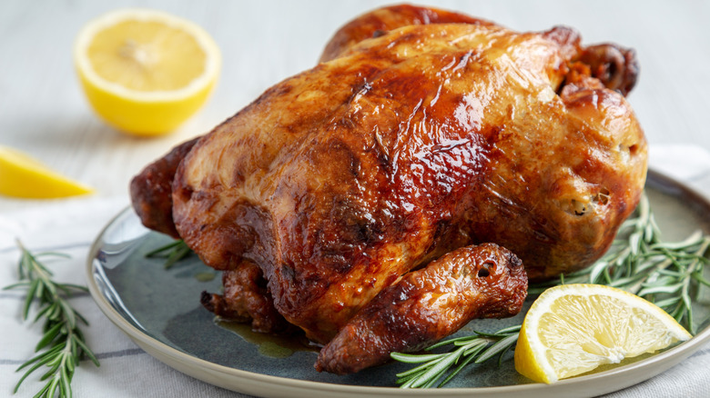 Rotisserie chicken on a plate with lemon and rosemary garnish
