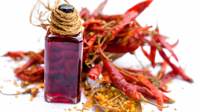 A bottle of chili extract surrounded by hot red chilis