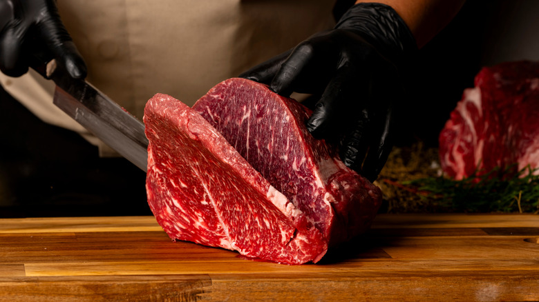 A chef with black latex gloves slicing beef