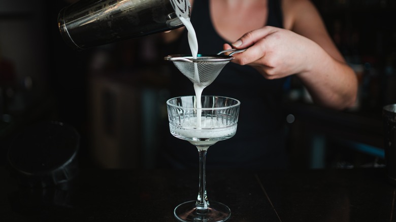 bartender straining cocktail into glass