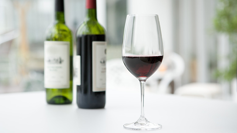 Glass of wine sits on a table with two bottles in the background