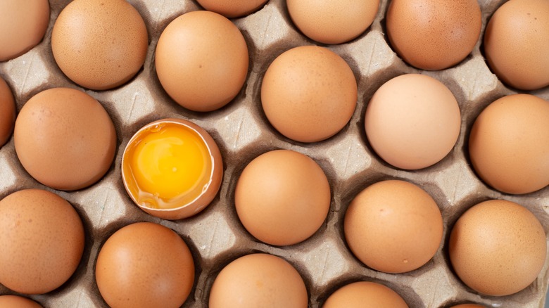 up-close photo of brown eggs with one egg cracked showing the yellow yolk