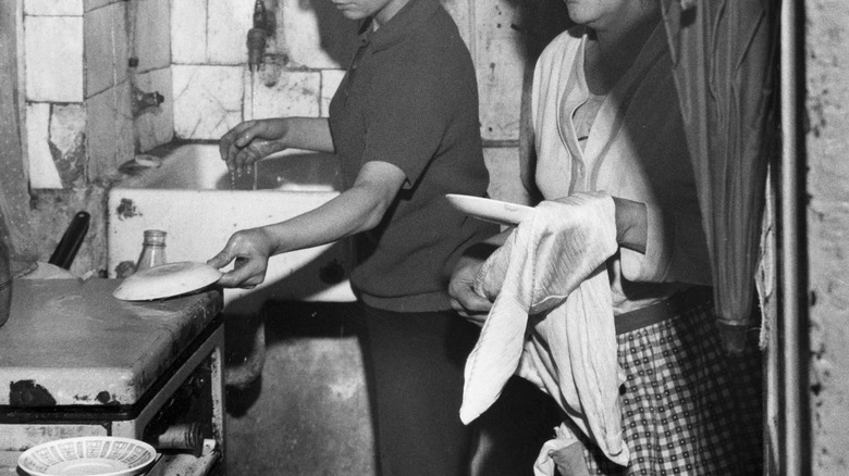 Two people dry dishes in a black and white photograph
