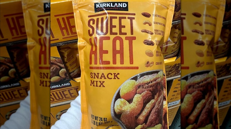 A bag of Kirkland Sweet Heat snack mix being held in front of a Costco store on a sunny day