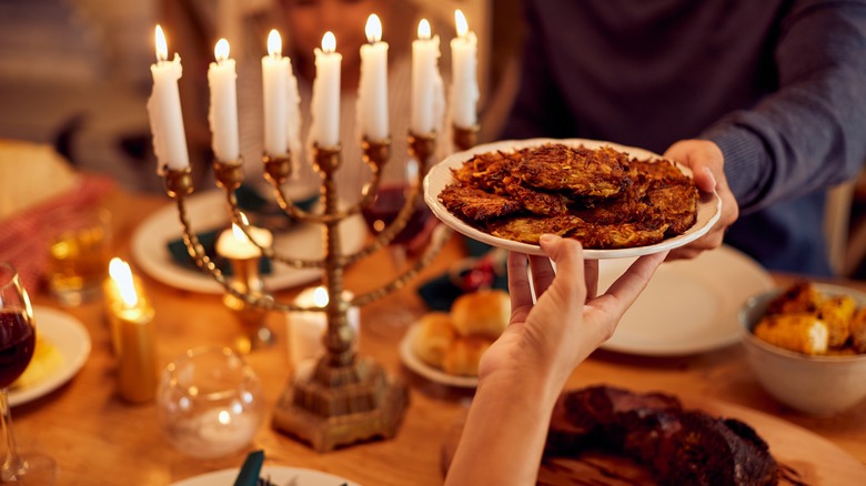 People passing latkes next to menorah