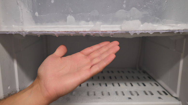 Hand gesturing at an empty freezer with ice buildup