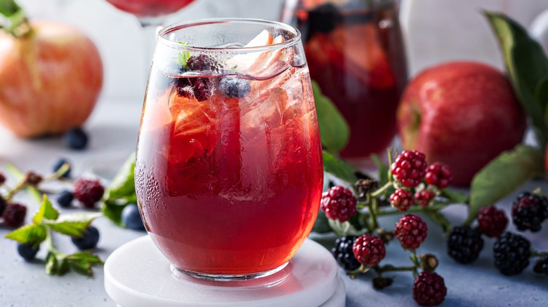 Stemless glass of red sangria surrounded by apples and berries