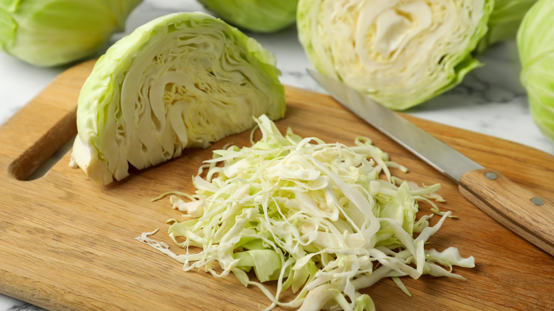 Quartered cabbage by sliced cabbage on cutting board with knife.