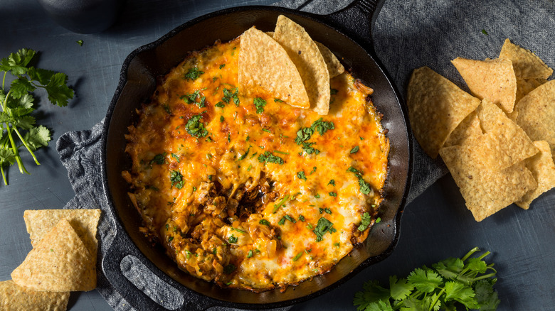 Skillet of homemade Mexican chorizo queso made with Oaxaca cheese next to herbs and tortilla chips