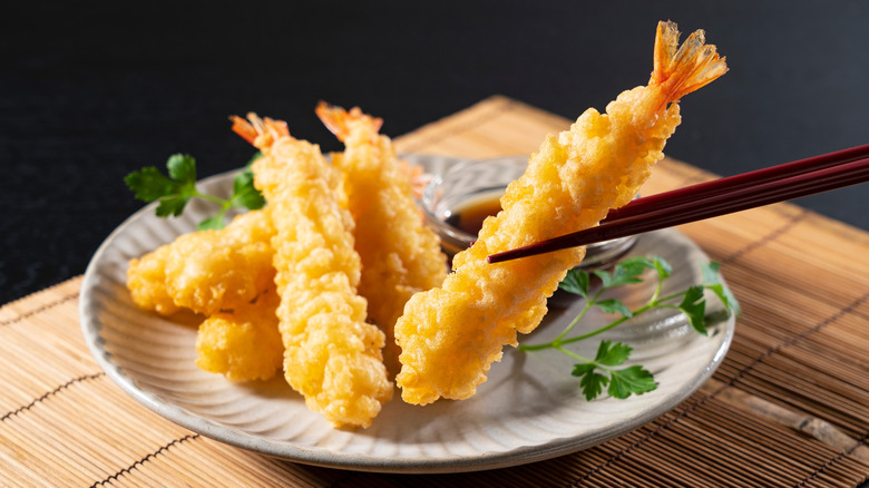 light and crispy tempura shrimp on a plate with one piece being held in chopsticks
