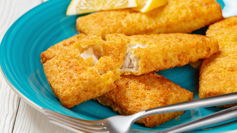 Breaded Alaskan pollock on a blue plate with a lemon wedge and fork