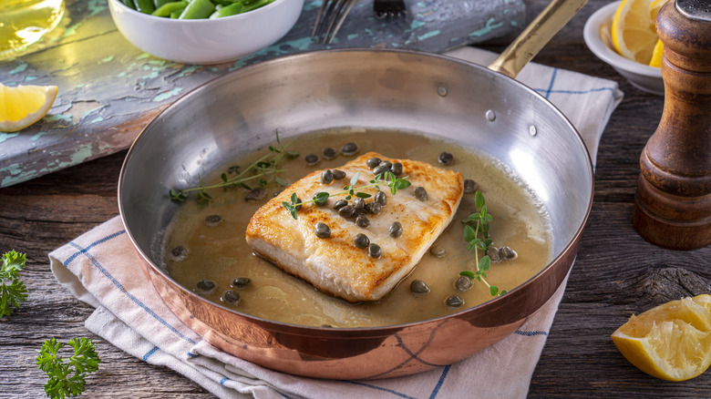 a filet of halibut in a copper frying pan with butter and capers