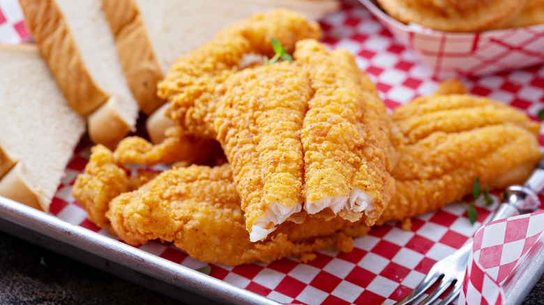 Deep-fried catfish filets on a metal tray with bread